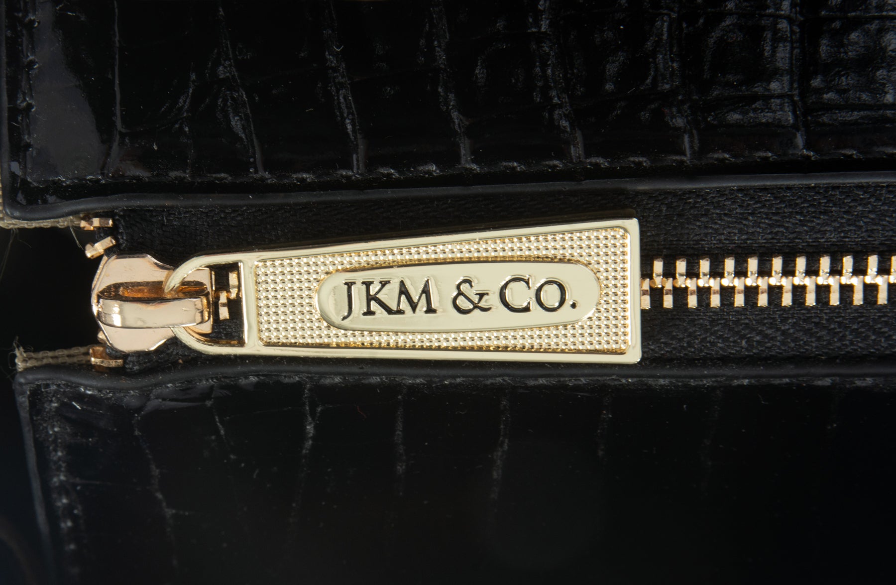 A gold zipper pull branded with the company's logo in an elegant font with a textured background. This durable YKK zipper secures the interior of the bag to protect your belongings as you commute to and from work or set off on an important business trip.
