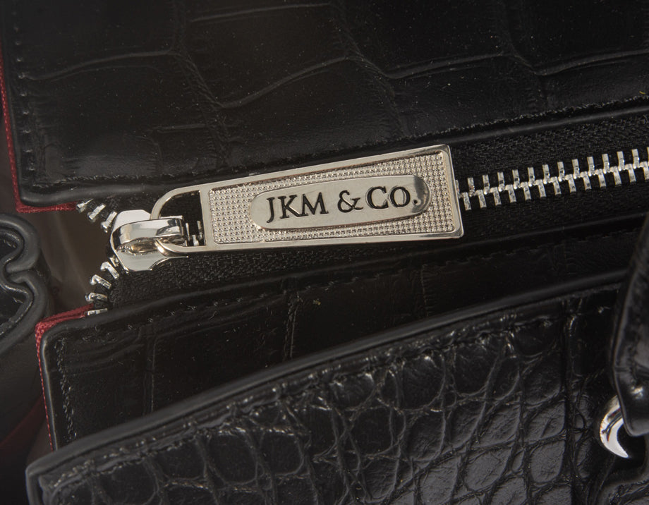 Close-up of high-quality zippers, featuring a personalized metal zipper pull engraved with the JKM and Company logo. A stylish, durable detail that enhances both function and elegance. The interior fabric is a bright pop of color against the black.
