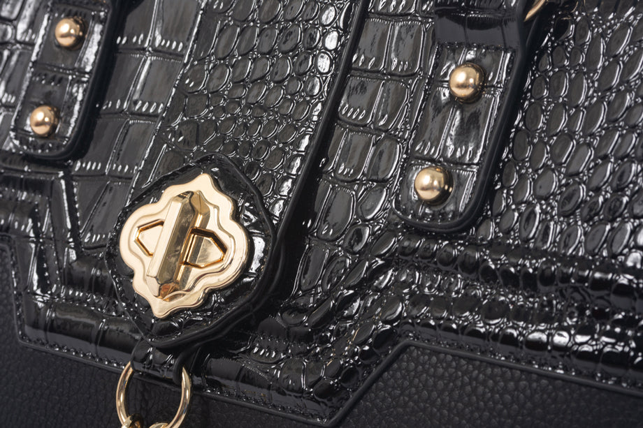 Close-up of a black rolling computer bag with elegant gold metal accents, including a gold twist pendant. The bag showcases good quality fabric and craftsmanship, combining style and functionality for a refined work or travel accessory.